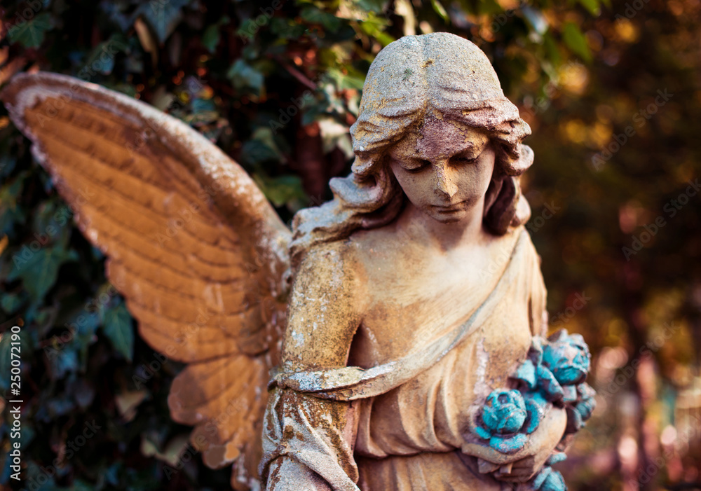A fragment of ancient sculpture angel in a golden glow in the old cemetery. Symbol of love, invisible forces, purity, enlightenment, ministry. Chariot. Retro vintage style.