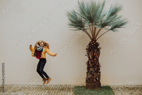 A beautiful young tanned girl jump near a yellow wall in the south. Fashionable dress, bright make-up, tan. Palms, photo
