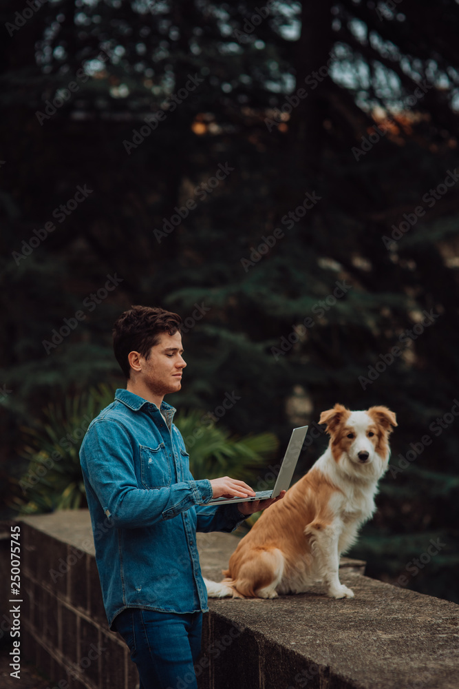 Man in jeans suit with red dog border collie standing with a laptop in garden