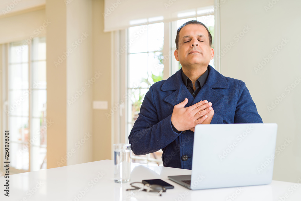 Middle age business man working using laptop smiling with hands on chest with closed eyes and grateful gesture on face. Health concept.