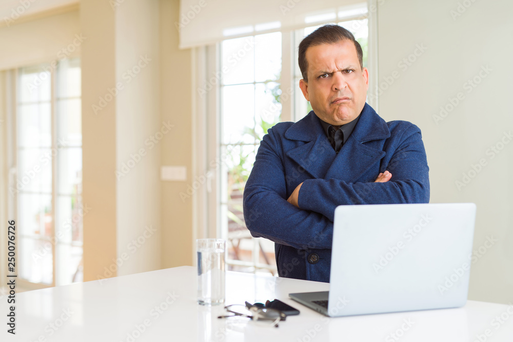 Middle age business man working using laptop skeptic and nervous, disapproving expression on face with crossed arms. Negative person. Middle age business man working using laptop skeptic and nervous, disapproving expression on face with crossed arms. Negative person.