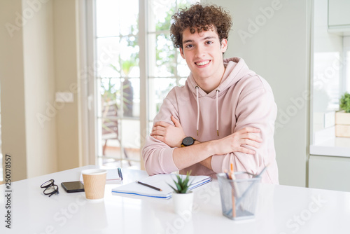 Young student man writing on notebook and studying happy face smiling with crossed arms looking at the camera. Positive person.