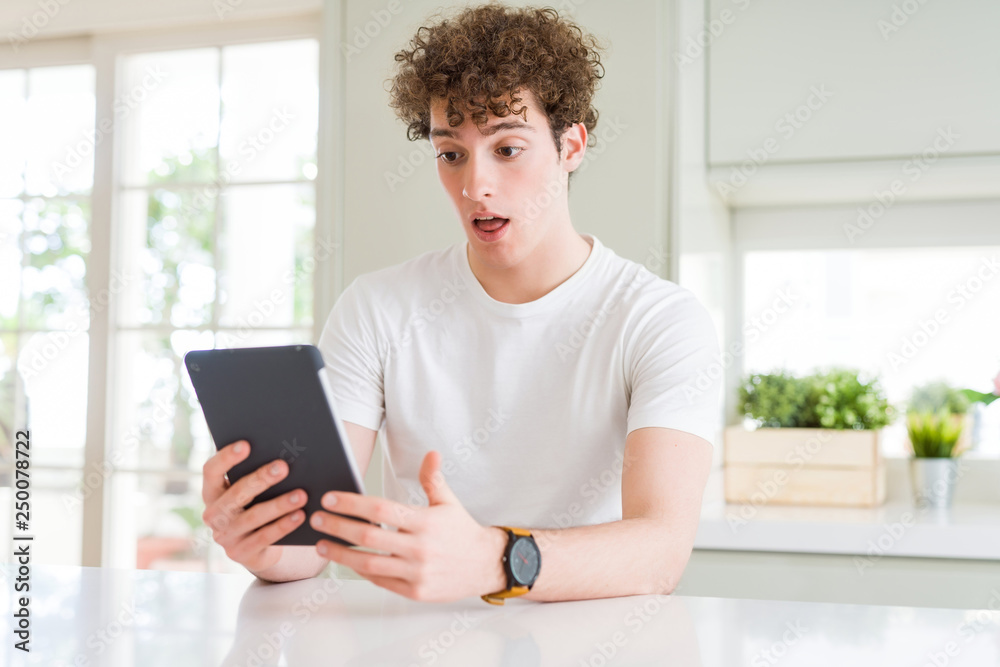 Young man using touchpad tablet scared in shock with a surprise face, afraid and excited with fear expression