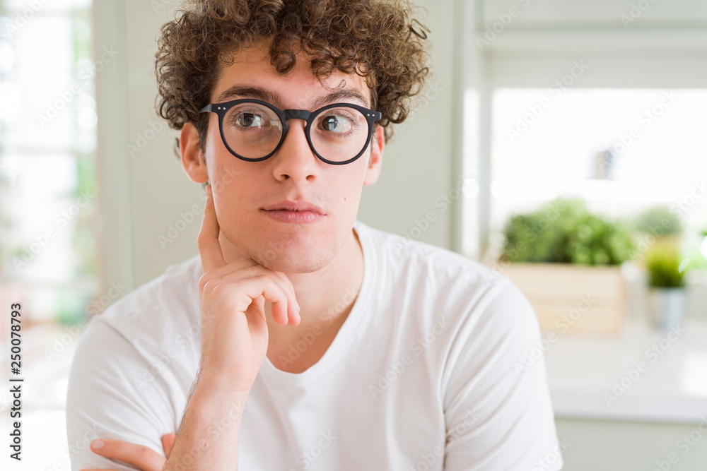 Young handsome man wearing glasses with hand on chin thinking about question, pensive expression. Smiling with thoughtful face. Doubt concept. Young handsome man wearing glasses with hand on chin thinking about question, pensive expression. Smiling with thoughtful face. Doubt concept.
