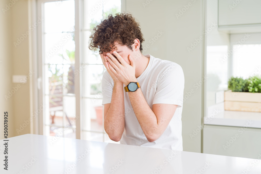 Fototapeta premium Young handsome man wearing white t-shirt at home with sad expression covering face with hands while crying. Depression concept.