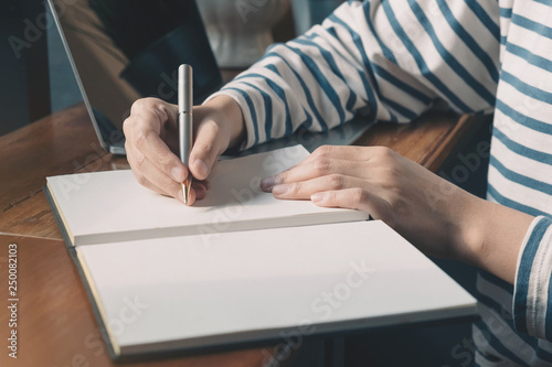 Close up. Asian Female writing on a notebook with computer laptop in the coffee shop.