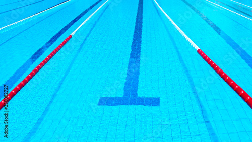 Swimming pool with marked red and white lanes. Empty swimming pool without people with quiet standing water of blue and azure shades. Background for water sports with a lot of space for text.