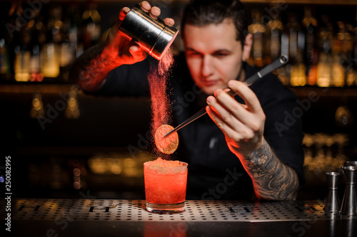 Professional bartender adding to an alcoholic cocktail a dried orange and powder