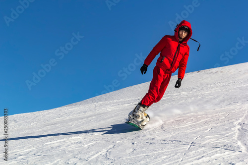 snowboarder quickly rolls down the mountain in loose snow against a blue sky on a sunny day. Copy space