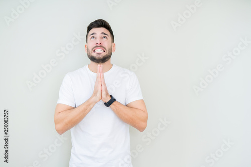 Young handsome man wearing casual white t-shirt over isolated background begging and praying with hands together with hope expression on face very emotional and worried. Asking for forgiveness