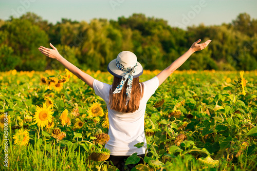 Young woman with long hair in sunflower Field with hands up. Beauty girl outdoors enjoying nature