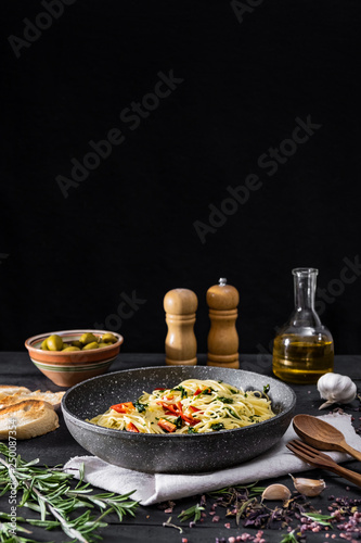 Pan of cooked italian pasta, copy space. Traditional spaghetti meal with vegetables and olives on black rustic background