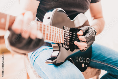 фотографія Rocker in black T-shirts and jeans playing hard rock on a left-handed black elec
