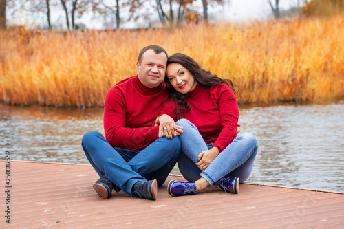 Married couple sitting on pier on background of autumn lake