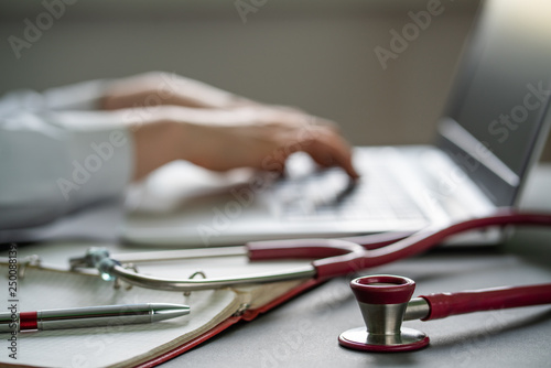 Stethoscope and background doctor using laptop at desk in clinic