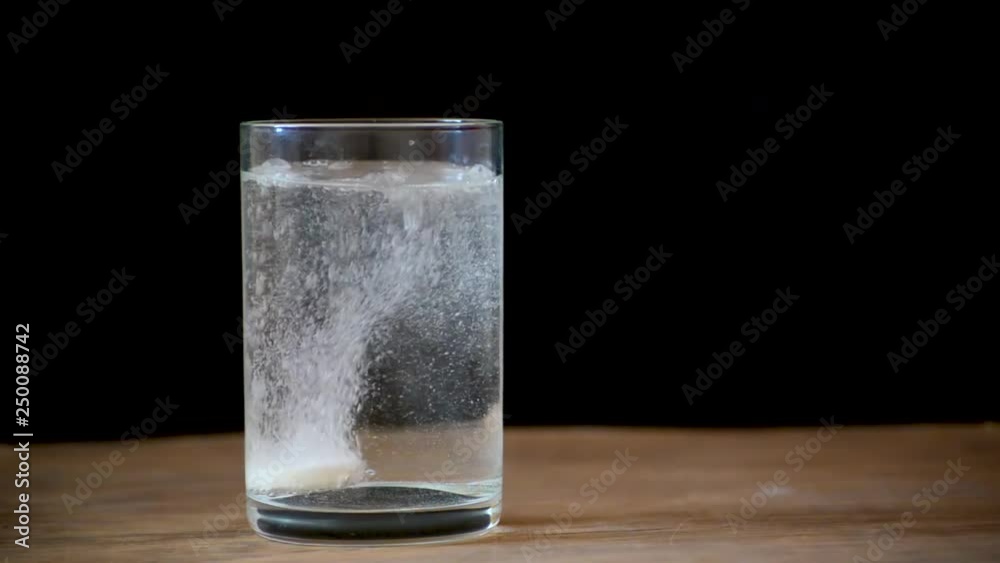 The girl throws a white effervescent tablet into a glass of water on the table. The girl throws a white effervescent tablet into a glass of water on the table.