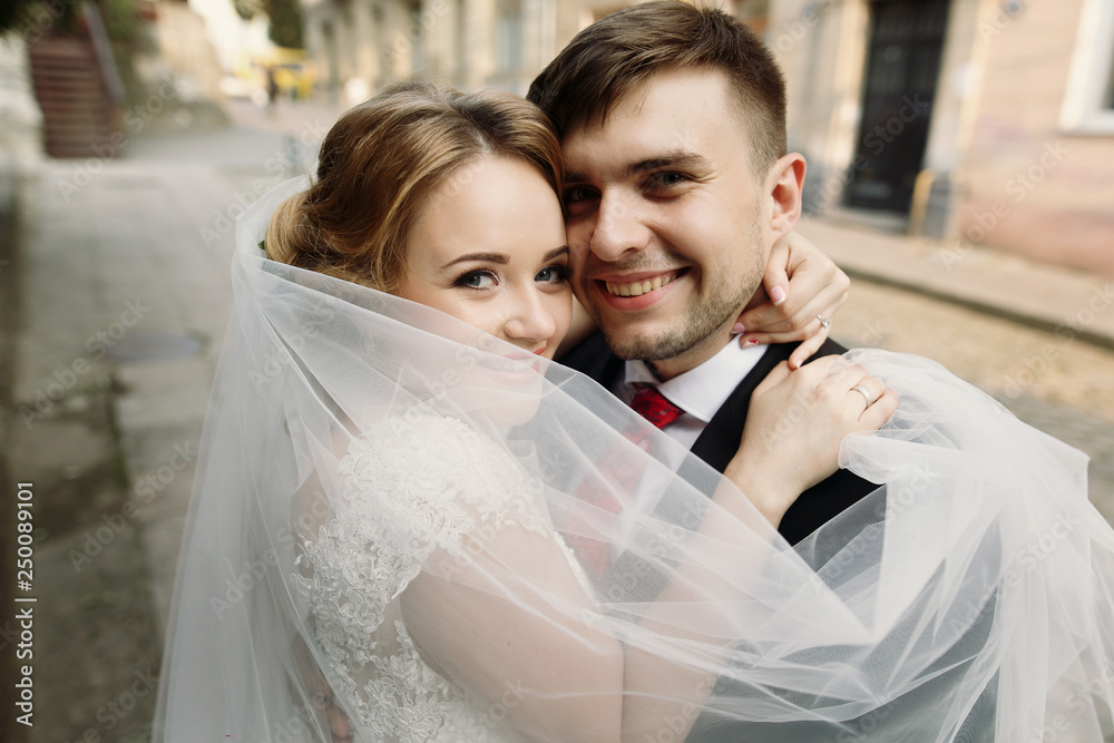 Naklejka premium Cheerful bride and groom hugging face closeup, newlywed couple smiling in embrace outdoors, family portrait concept