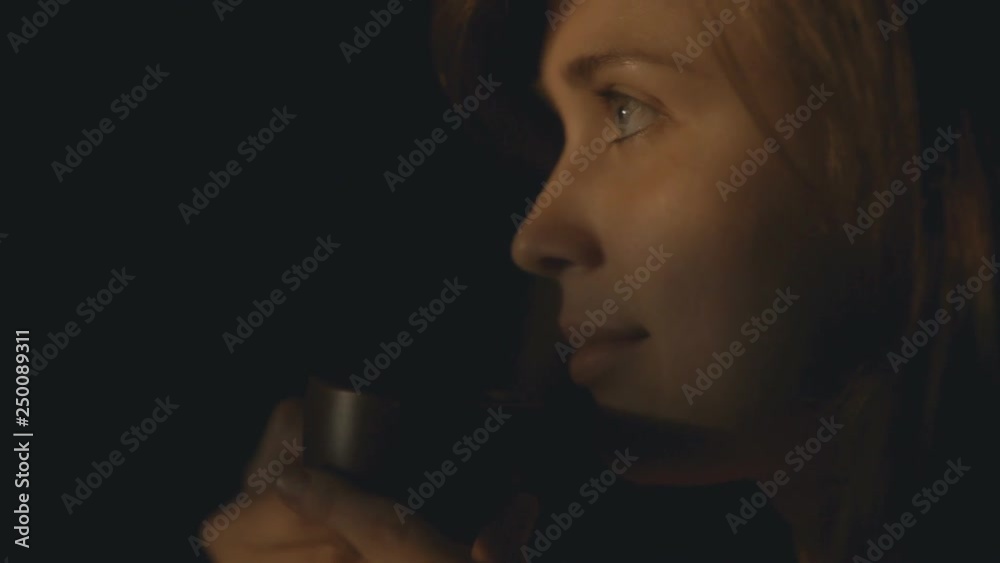 Profile of a young woman drinking coffee in front of the window, the girl’s face is illuminated by the sunset sun while drinking a hot drink at home. Profile of a young woman drinking coffee in front of the window, the girl’s face is illuminated by the sunset sun while drinking a hot drink at home.