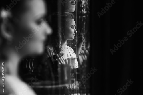 Gorgeous blonde bride posing near mirror, reflection of sexy woman in stylish robe sitting in front of fairytale mirror, morning wedding preparation, face closeup