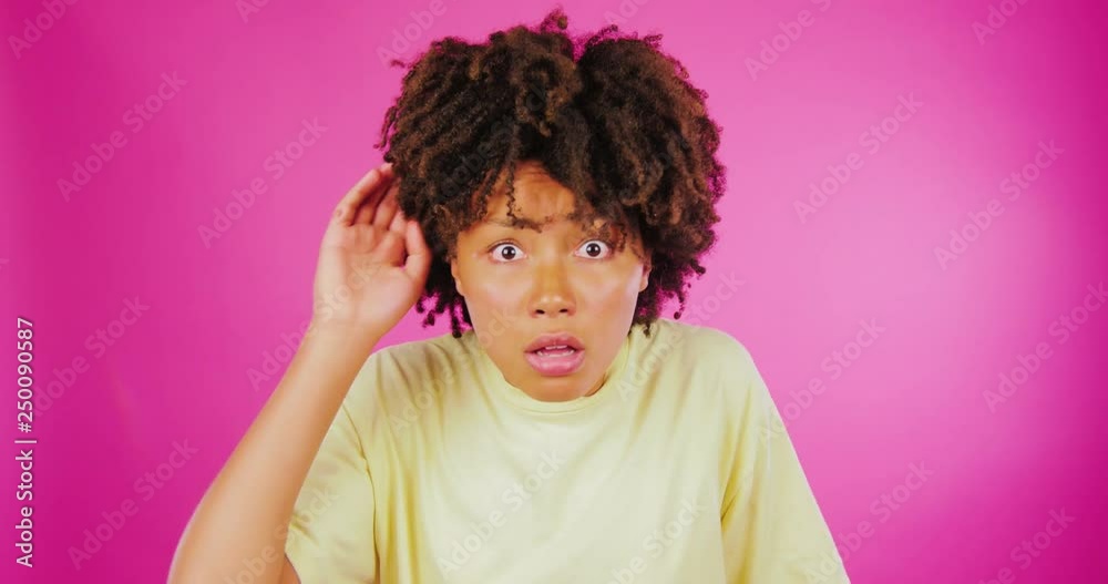 A young curly African girl is outraged, complains, indignant on a pink background.