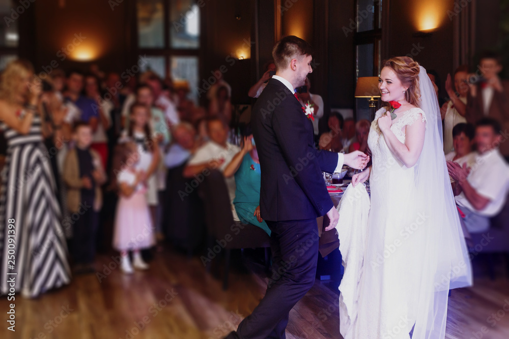 Romantic bride and groom dancing and holding hands at wedding reception in restaurante, newlywed couple first dance at evening party, guests looking in the background Romantic bride and groom dancing and holding hands at wedding reception in restaurante, newlywed couple first dance at evening party, guests looking in the background