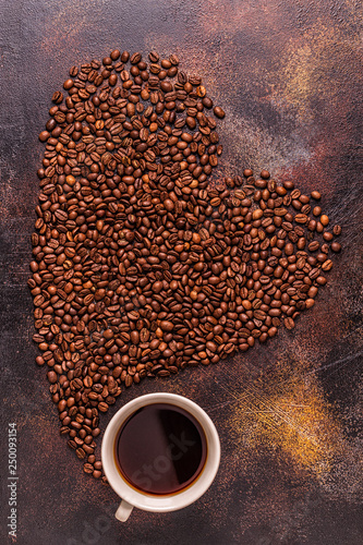A cup of coffee and coffee beans poured in the form of a heart