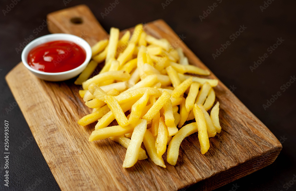 French fries with ketchup on a cutting board, background is concrete French fries with ketchup on a cutting board, background is concrete