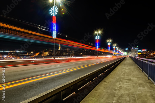 Belgrade, Serbia - February 10, 2019: Belgrade waterfront and "Branko" bridge on the Sava River. Panorama of Belgrade by night with reflection. There are traces of the vehicle on the photo.