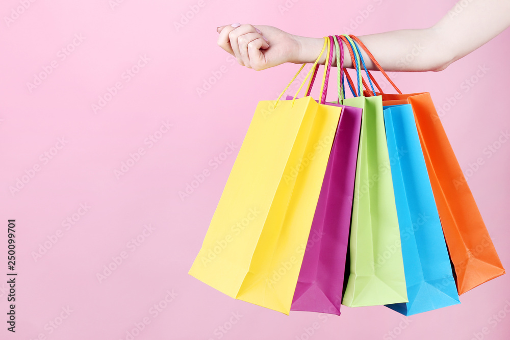 Female hand holding colorful shopping bags on pink background