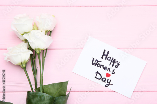 Text Happy Women's Day with eustoma flowers on pink wooden table