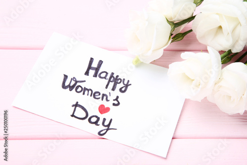 Text Happy Women's Day with eustoma flowers on pink wooden table