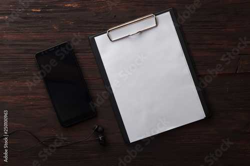 Clipboard with white paper phone and headphones on wooden background