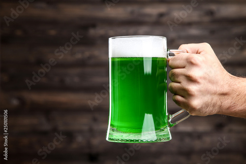 St. Patrick's Day. Glass mug with green beer in male hand on wooden background