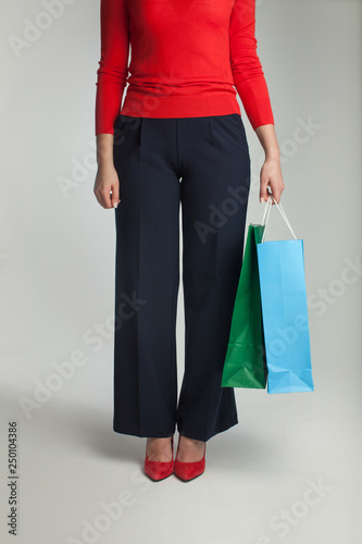 Beautiful elegant woman in red sweater and navy blue pants with shopping packages in hand.