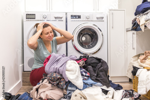 Upset woman in laudry room sitting ona floor with dirty clothes photo