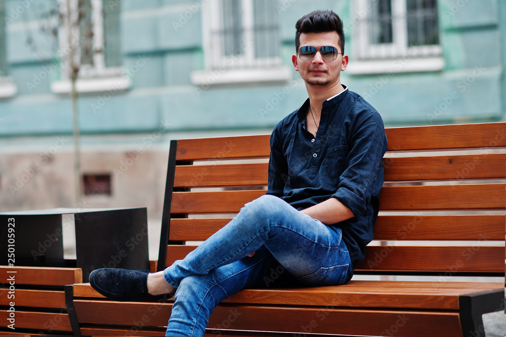 Stylish indian model man in casual clothes, black shirt and sunglasses  posed outdoor at street of India and sitting on bench. Stock-Foto | Adobe  Stock