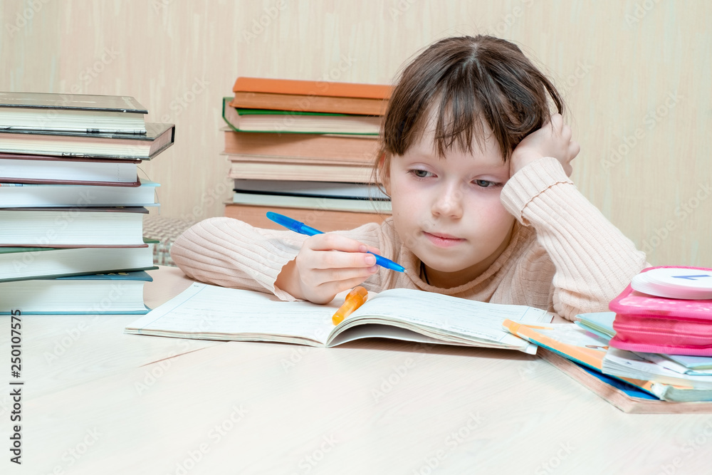 A tired child sits behind a notebook with half-closed eyes. The schoolboy rests his head on one arm. In the right hand the child holds a fountain pen. A tired child sits behind a notebook with half-closed eyes. The schoolboy rests his head on one arm. In the right hand the child holds a fountain pen.