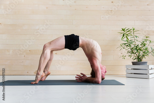 Sporty man practicing yoga on yoga class, bridgepose photo