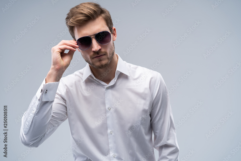 portrait of a young fashion man wearing sunglasses on grey background. portrait of a young fashion man wearing sunglasses on grey background.
