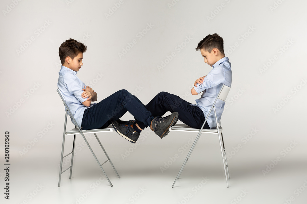 Obraz premium Serious brothers teenagers sitting on chairs against each other