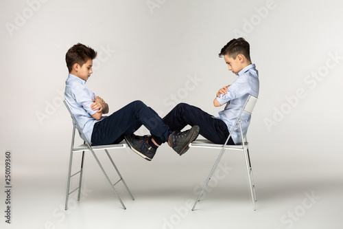 Serious brothers teenagers sitting on chairs against each other