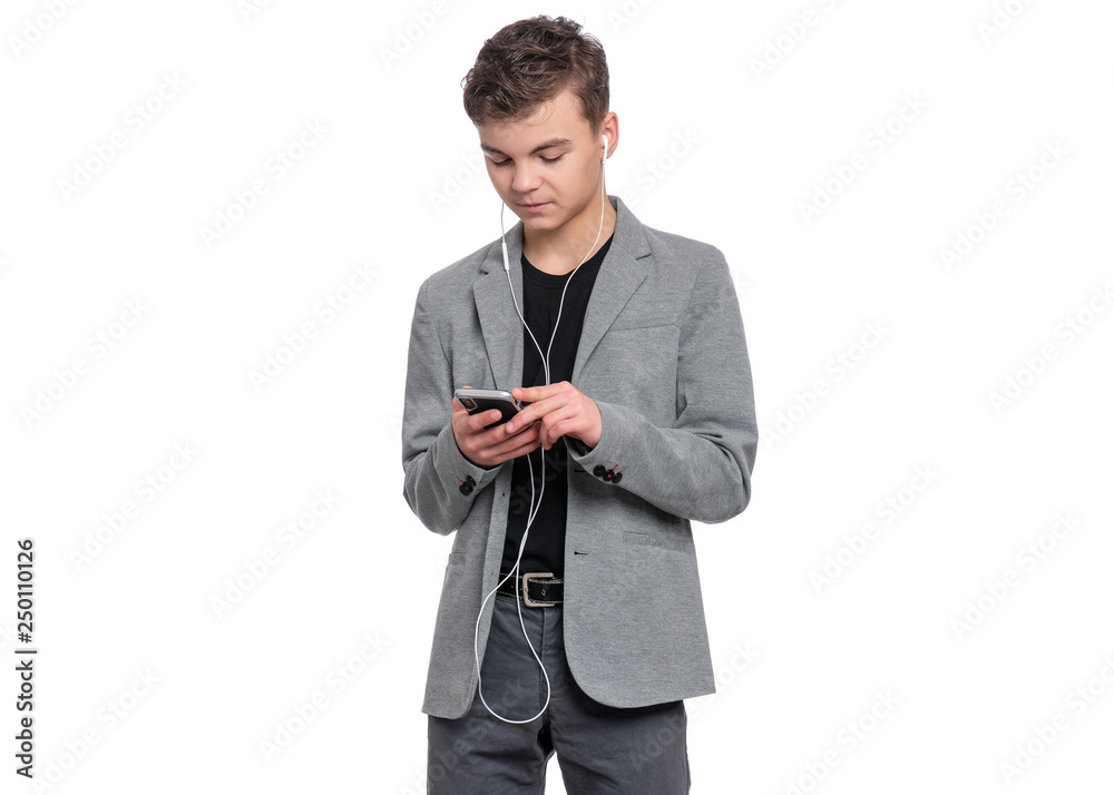 Portrait of Handsome Teen Boy with Mobile Phone and Headphones, isolated on white background. Smiling Child playing on Smartphone and listening to music. Cute modern Teenager in suit. Portrait of Handsome Teen Boy with Mobile Phone and Headphones, isolated on white background. Smiling Child playing on Smartphone and listening to music. Cute modern Teenager in suit.