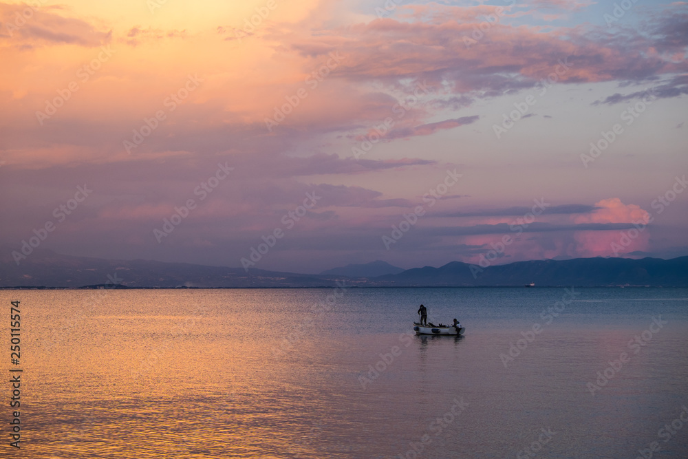 Lonely boat with two men in the sea with mountaibs and sunset clouds un the background. Shot in Gaeta - small mediterranean town in Italu