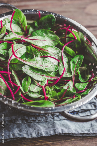 Fresh washed swiss chard leaves in a metal colander on a kitchen table. Preparation healthy vegan meals.