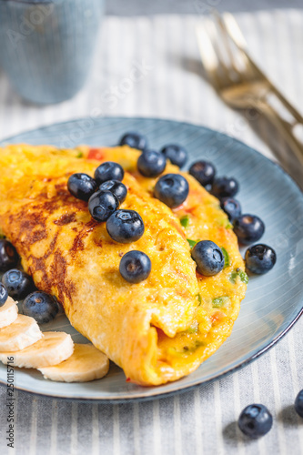 Vegetarian omelette with red and green bell peppers served with banana and fresh blueberry on a table.