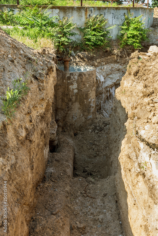 Deep trench with old rusty iron water pipes, prepared for dismantling of worn rusty water supply Deep trench with old rusty iron water pipes, prepared for dismantling of worn rusty water supply