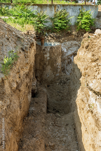 Deep trench with old rusty iron water pipes, prepared for dismantling of worn rusty water supply