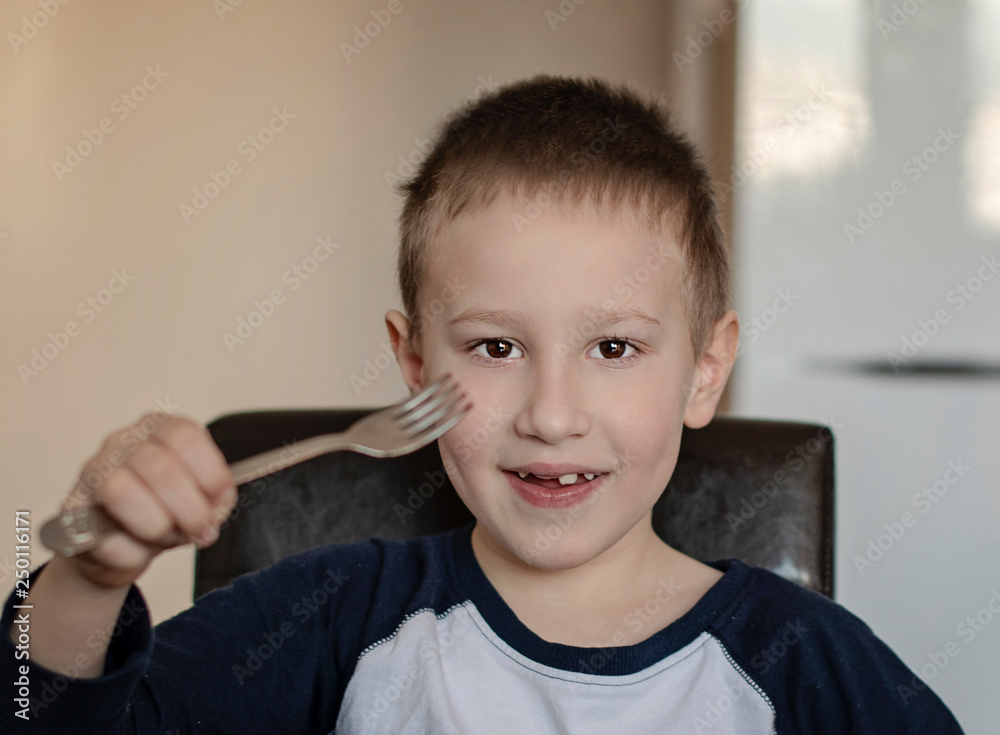 Close-up portrait of happy young pre-school boy eating with a fork in the kitchen at home. Close-up portrait of happy young pre-school boy eating with a fork in the kitchen at home.