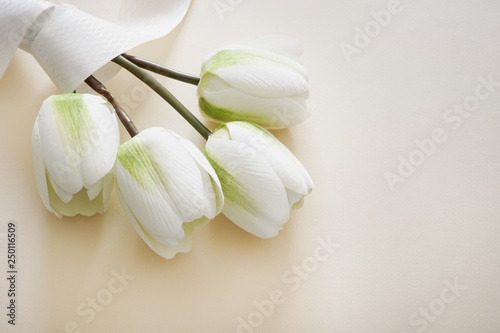 Beautiful bouquet of fake white tulips wrapped in ribbon in pastel background. Concept for Mother's Day with copy space.