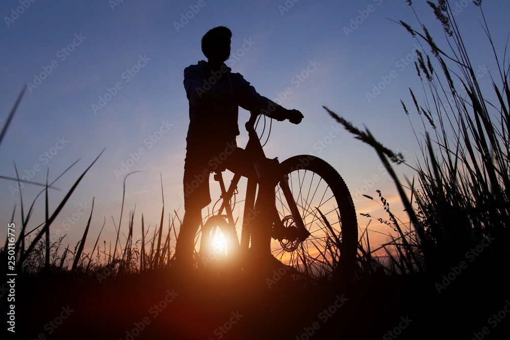 Obraz premium Silhouette of a cyclist against the sunset sky with sun and sunlight, copy space 